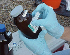 rubber gloved hands putting label on bottle